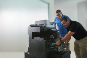 Two people from HGI working to fix a copier in an office.