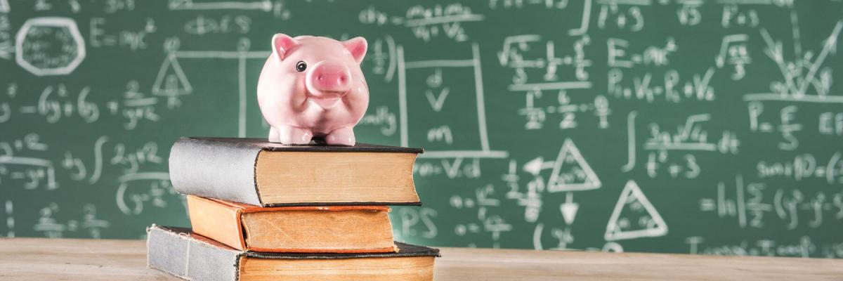 piggy bank on top of books in front of full chalkboard
