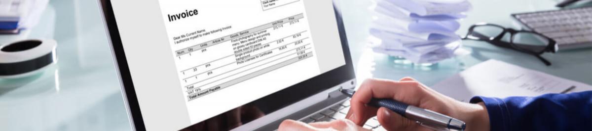 Close-up Of A Businessperson's Hand Analyzing Invoice On Laptop At Workplace