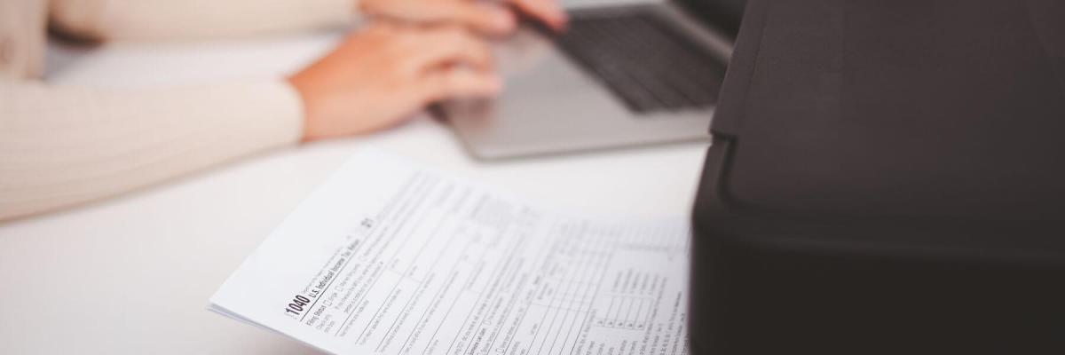 hands working on laptop next to printer with tax documents